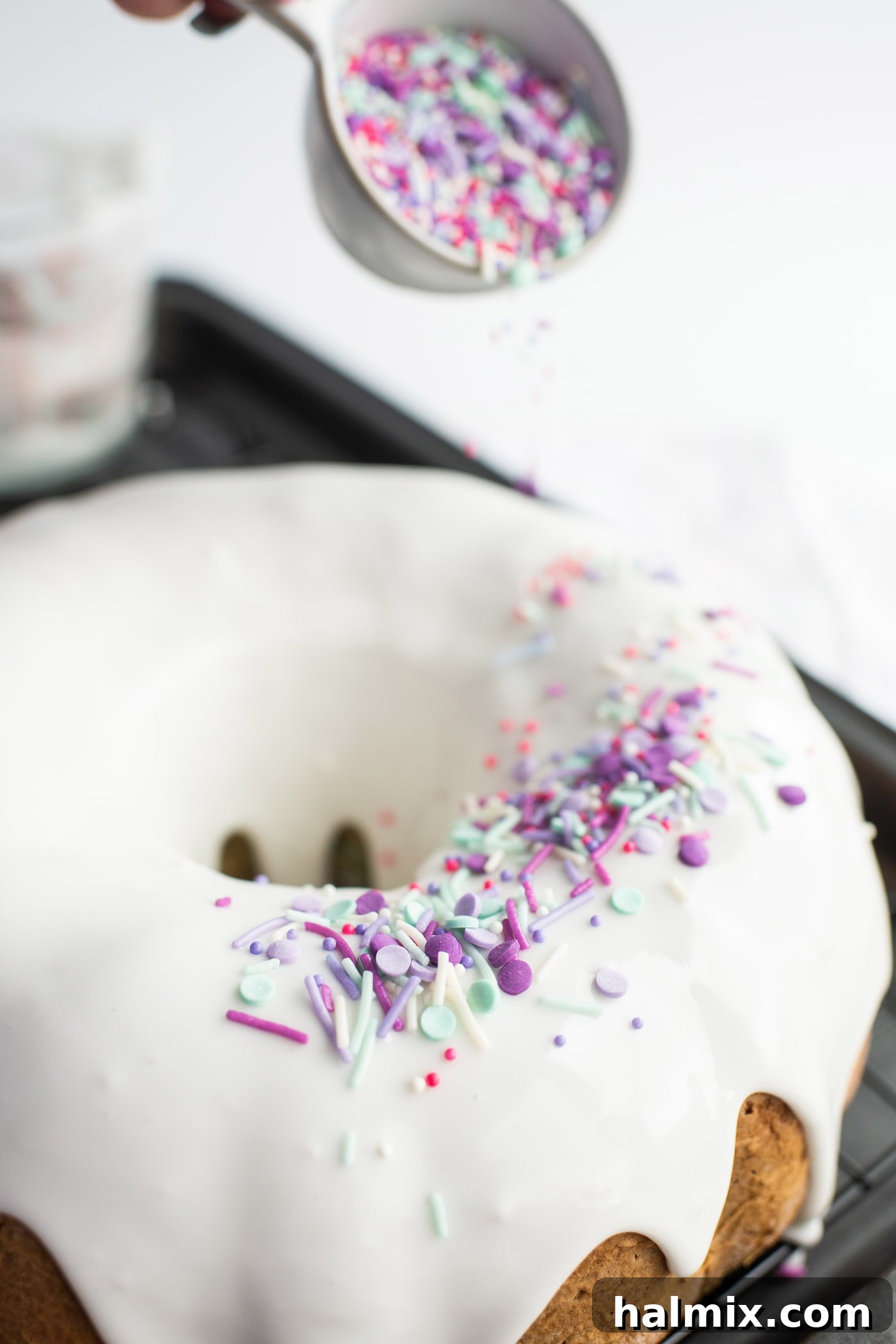 Decorating the glazed bundt cake with a generous amount of colorful sprinkles for a magical unicorn effect.