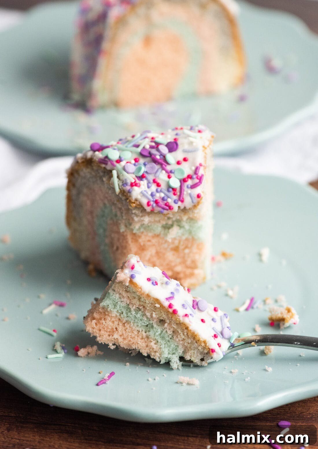 Close-up of a perfectly cut slice of Unicorn Bundt Cake on a white plate, revealing its beautiful rainbow interior layers and delicate crumb texture.