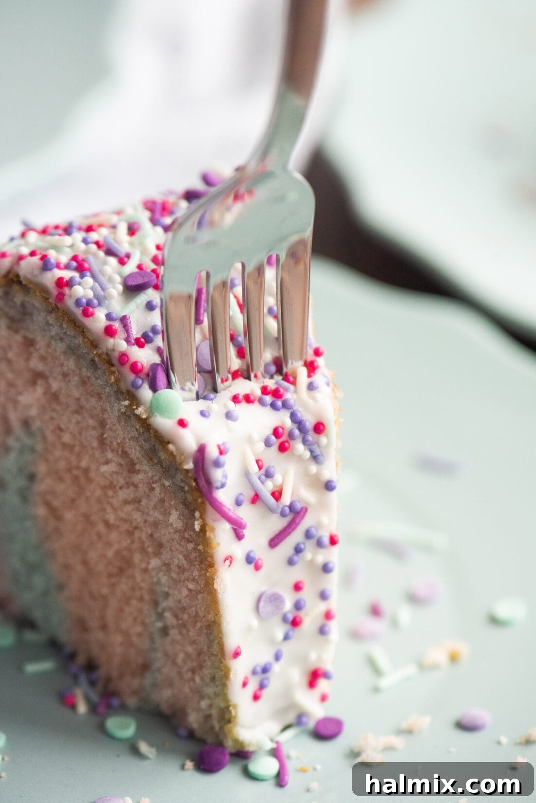 A fork taking a slice of Unicorn Bundt Cake, revealing the soft, colorful layers and the glistening glaze.