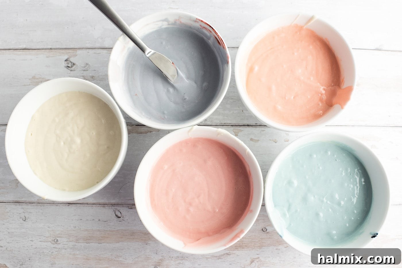 Cake batter divided into multiple bowls, each with a different pastel food coloring added, ready for the swirling process.