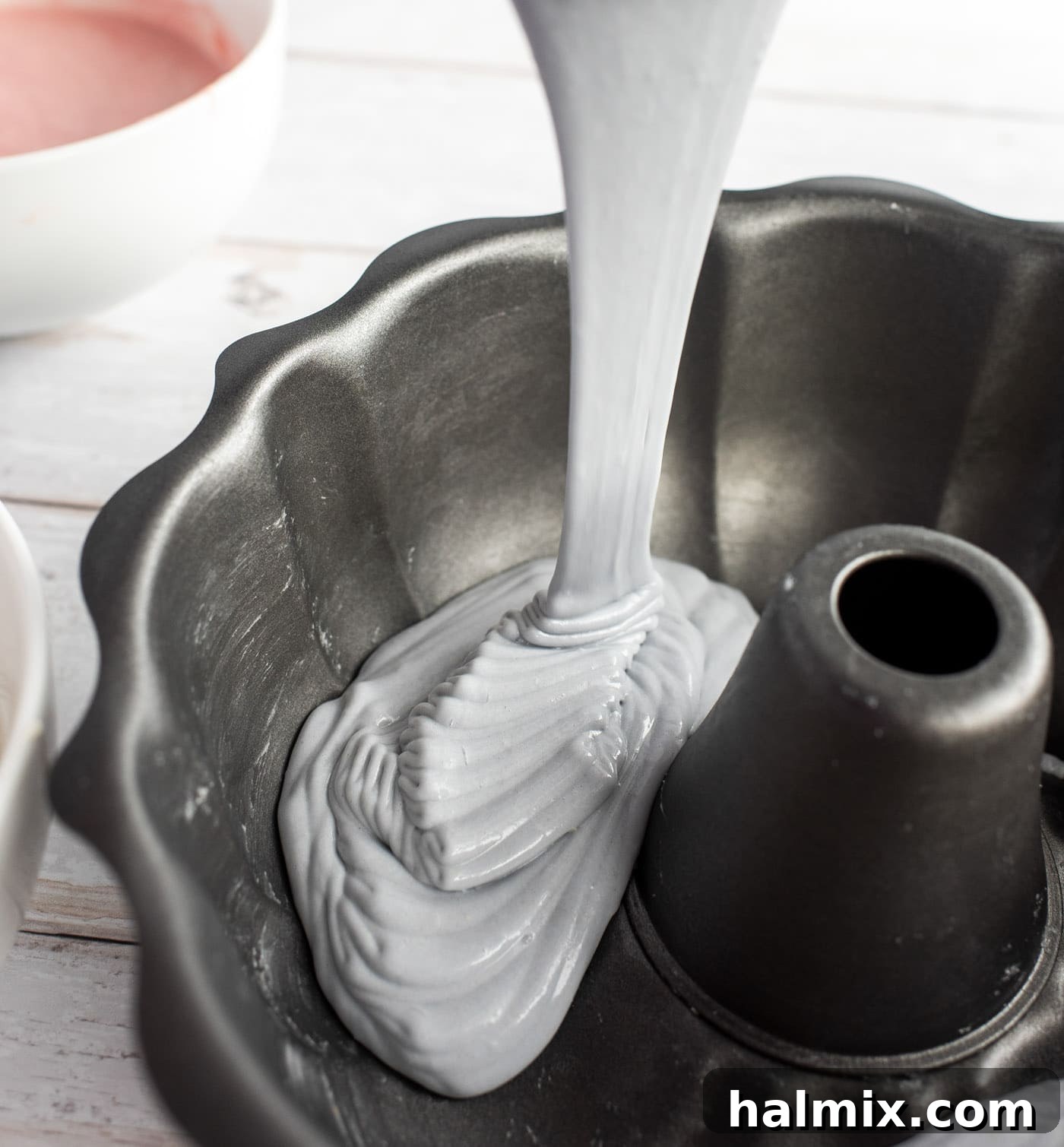 Pouring pastel purple cake batter into a greased bundt pan as the first layer of colors.