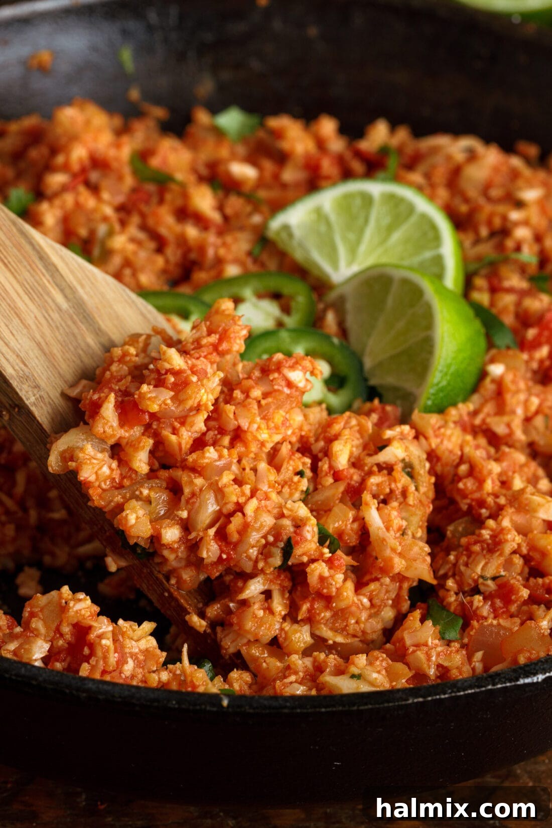 Zesty Mexican Cauli Rice 3 Scooping Mexican Cauliflower Rice with a wooden spoon, showcasing its vibrant color and texture