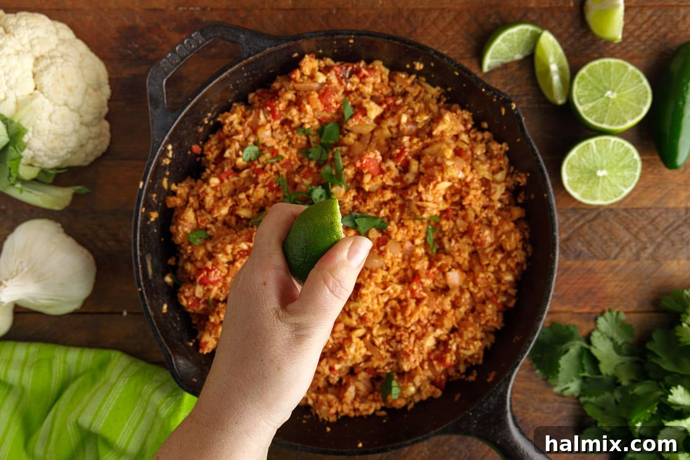 Squeezing fresh lime juice over a skillet of cooked Mexican Cauliflower Rice, garnished with cilantro.