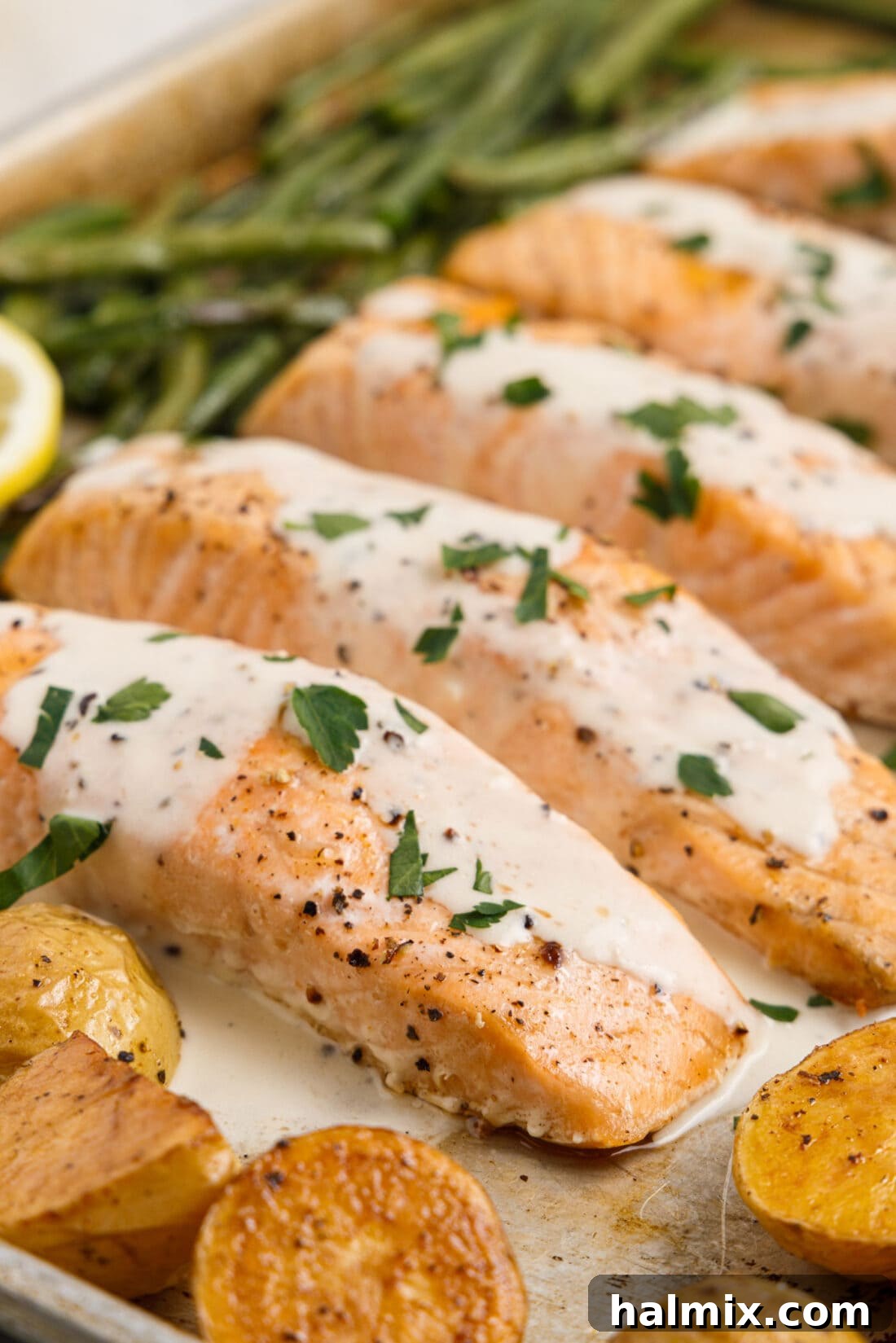 Baked Salmon with a vibrant lemon cream sauce drizzled over it, garnished with fresh herbs.