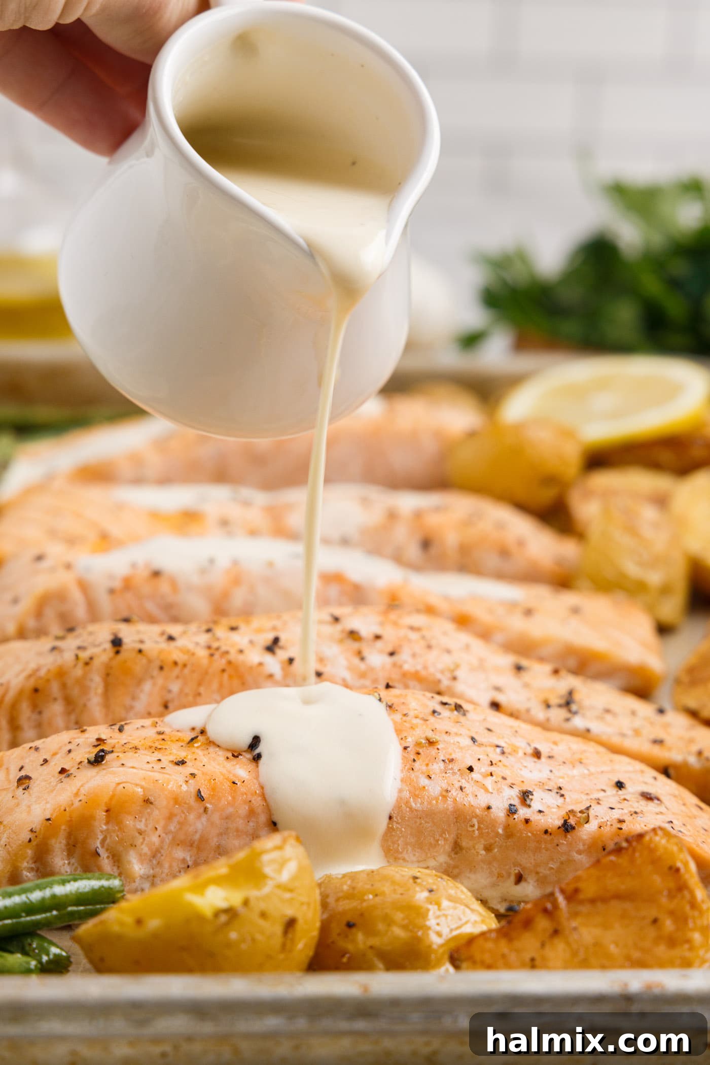 Pouring rich lemon cream sauce over freshly baked salmon fillets, ready to serve.