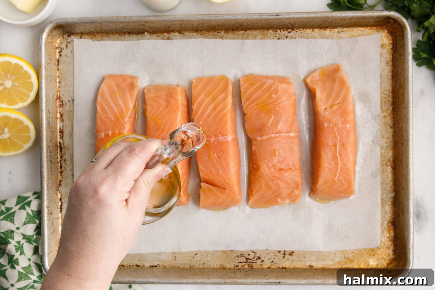 Drizzling olive oil over salmon fillets arranged on a parchment-lined baking sheet.