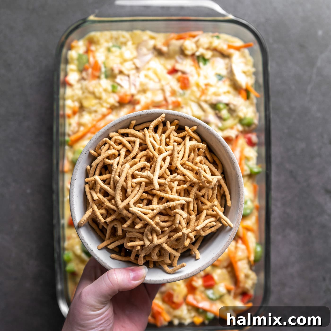 Crispy chow mein noodles are spread evenly over the top of the casserole mixture in the dish, prior to baking.