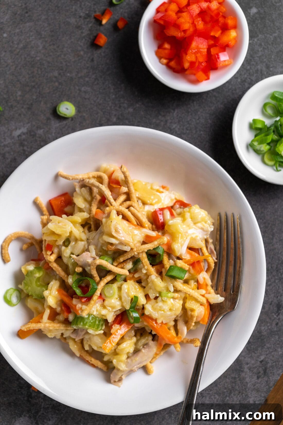A serving of Chicken Chow Mein Casserole on a white plate, garnished with green onions, showcasing its appetizing layers of chicken, rice, vegetables, and crispy noodles.