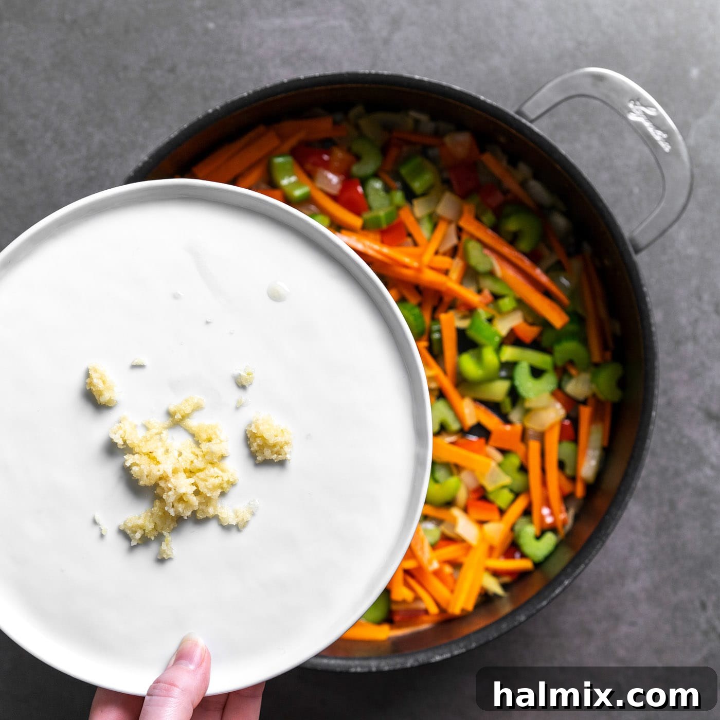 A small pile of minced garlic is carefully added to the sautéed vegetables in the skillet, ready to be stirred in.