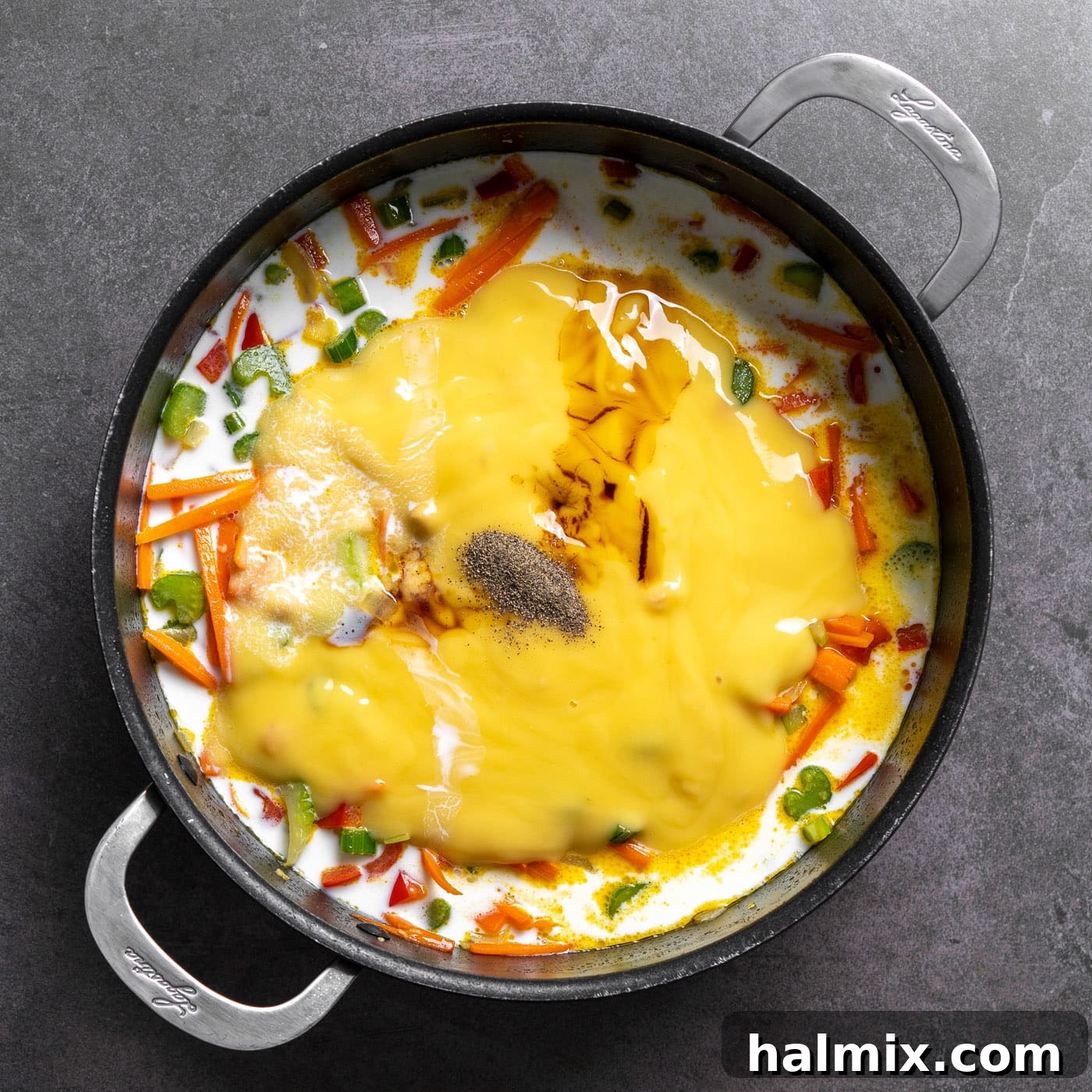 Condensed cream of chicken soup, milk, soy sauce, and black pepper are poured over the sautéed vegetables in the skillet.