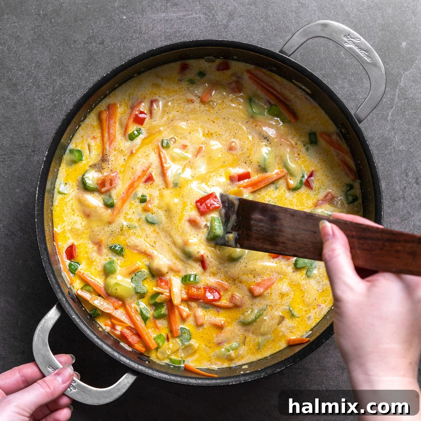 A spatula is used to stir the creamy sauce mixture with the vegetables in the pan until fully combined and smooth.