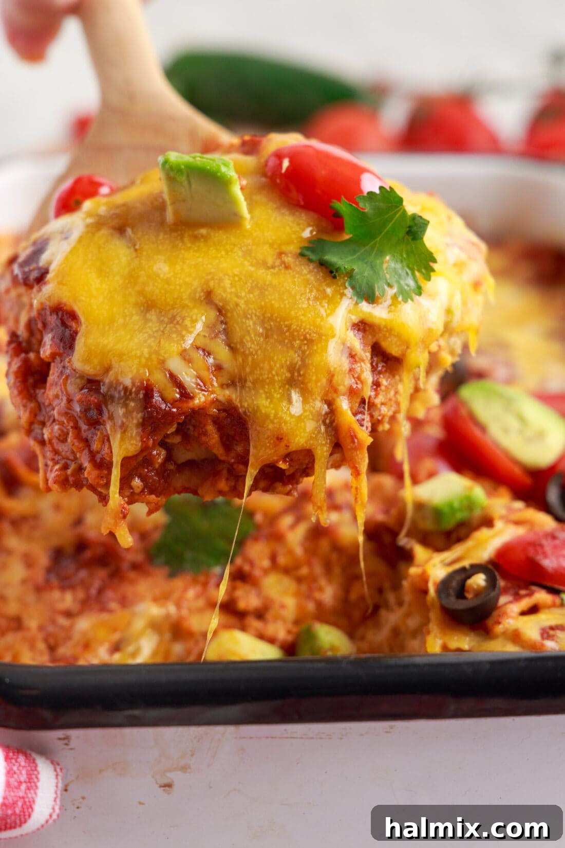 Lifting a spatula serving of bubbly Chicken Enchilada Casserole with melted cheese.