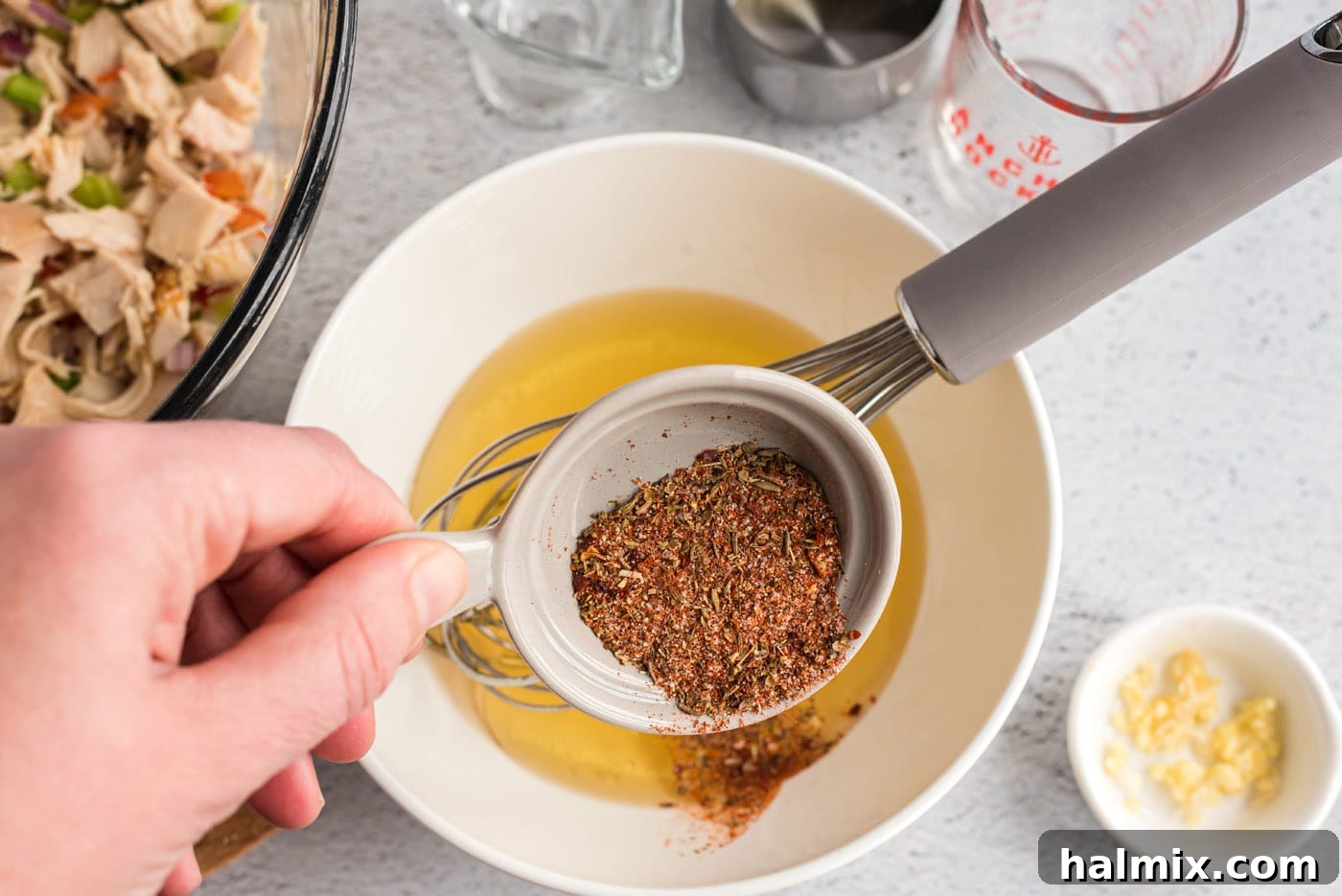 Olive oil, minced garlic, white vinegar, chicken broth, and Cajun seasoning in a bowl, before whisking
