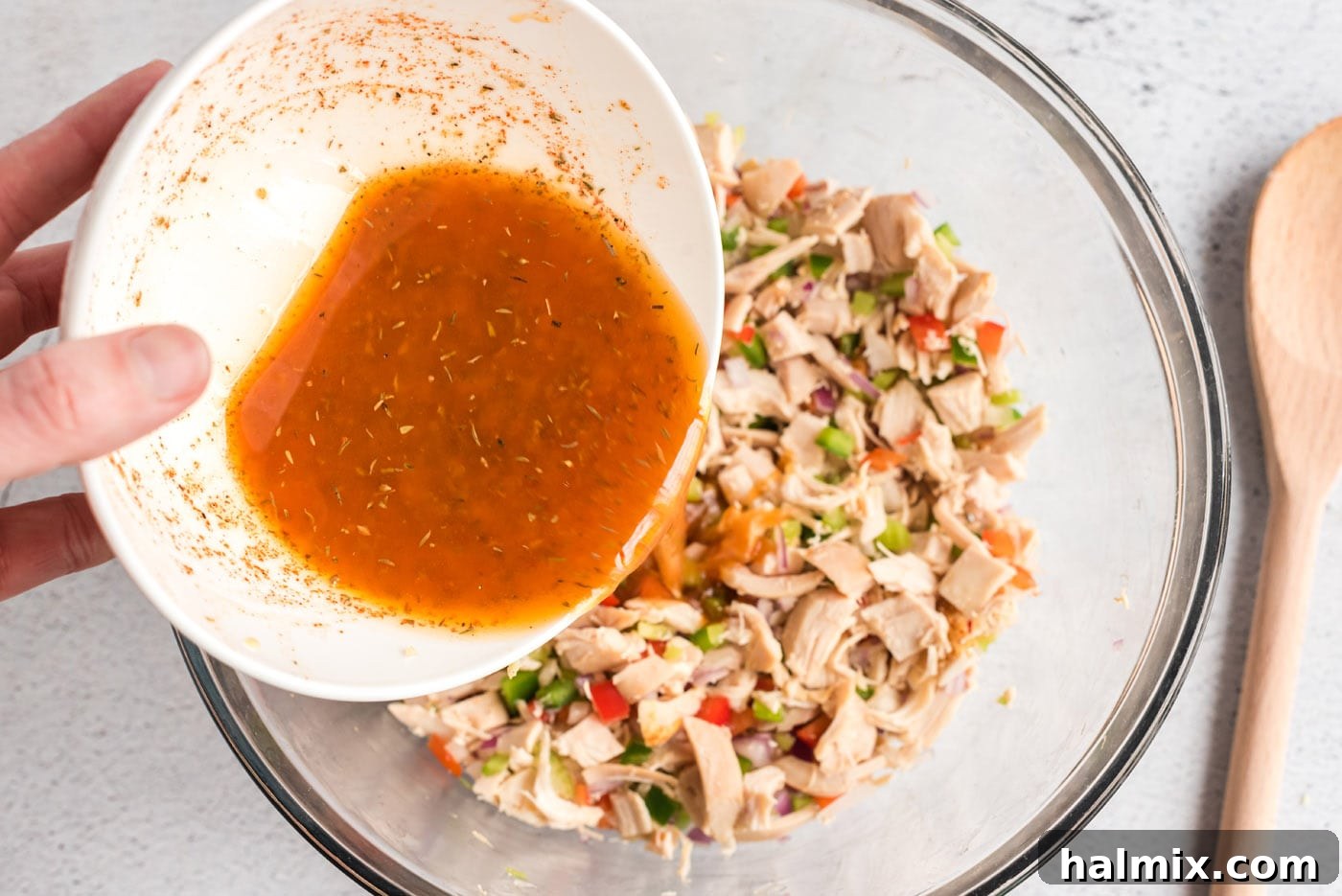 Pouring the freshly whisked Cajun dressing over the chicken and vegetable mixture in a bowl