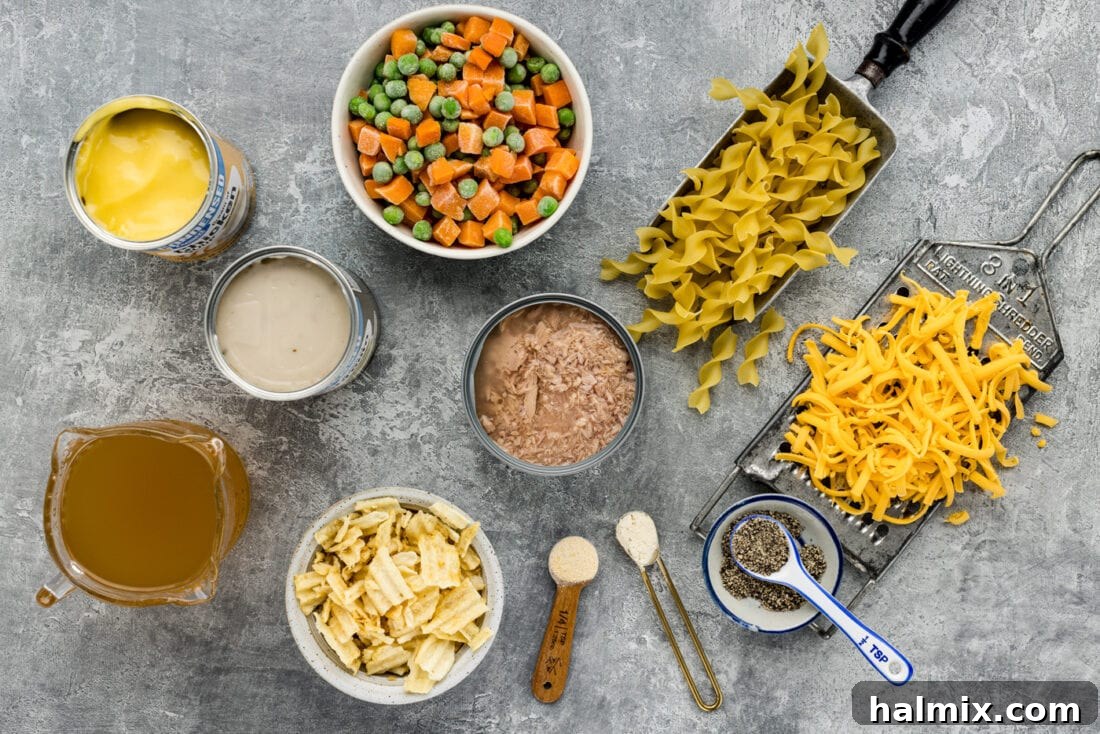 Creamy Tuna Bake 4 A flat lay of fresh ingredients for tuna casserole, including canned tuna, bags of frozen peas and carrots, cans of condensed soup, egg noodles, and various seasonings.