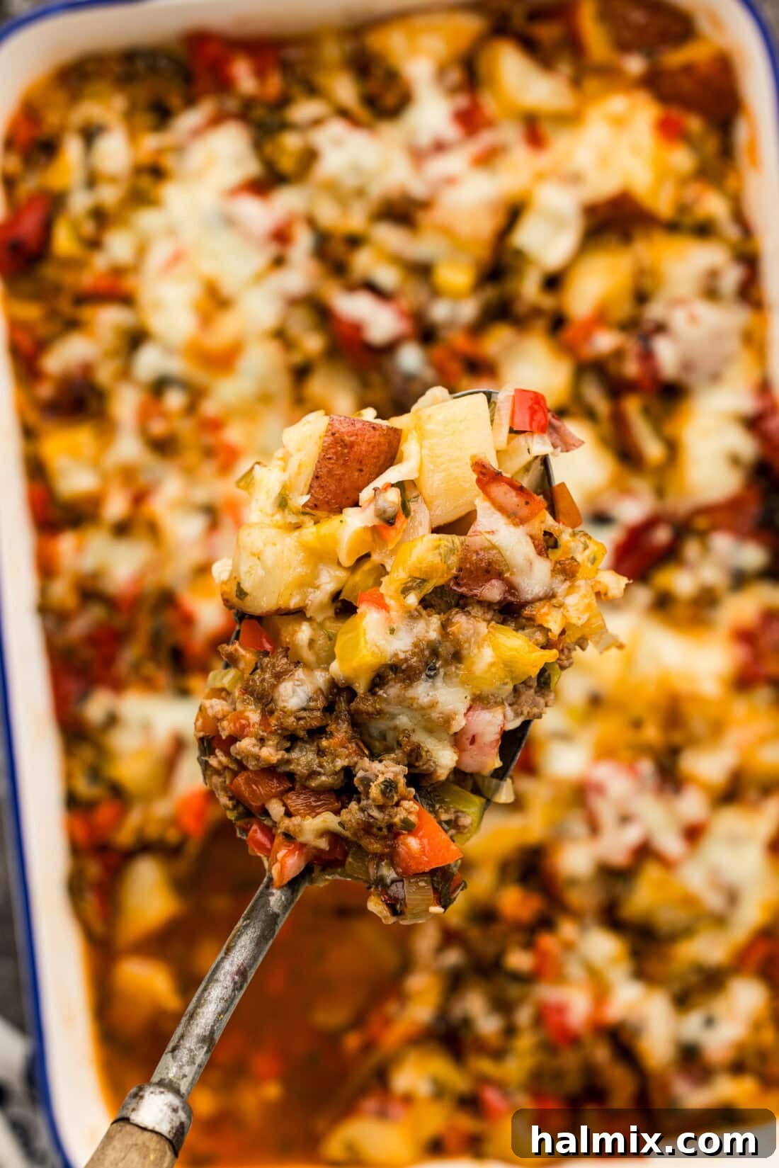 Hearty Sausage and Potato Bake 11 A generous spoonful of Sausage and Potato Casserole being held above the dish, ready to be served.