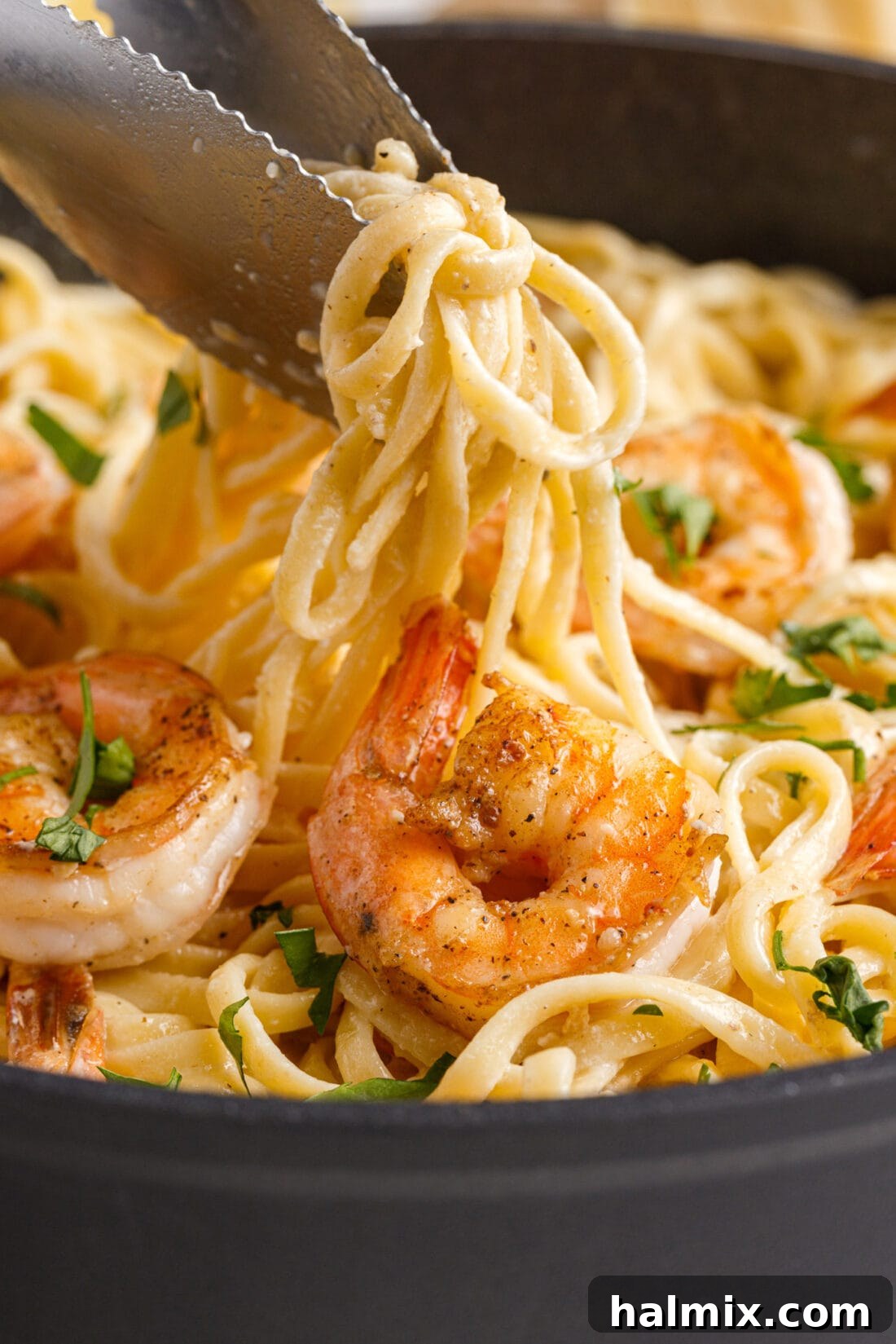 Creamy Garlic Shrimp Pasta 3 tongs lifting Shrimp Pasta from a skillet, showing the well-coated noodles and shrimp