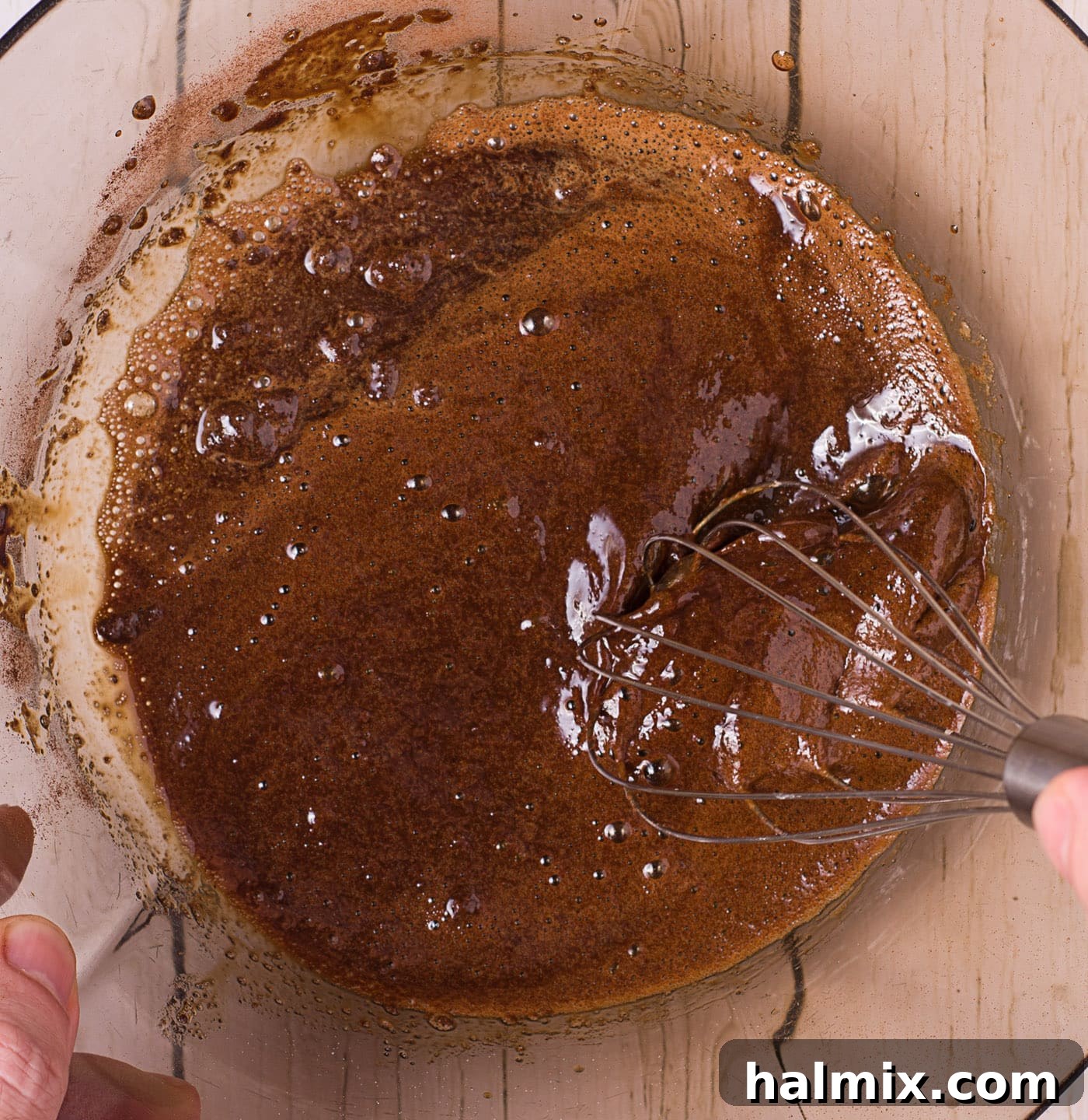 A person whisking instant coffee, water, and sugar in a bowl, showing the initial dark liquid stage.