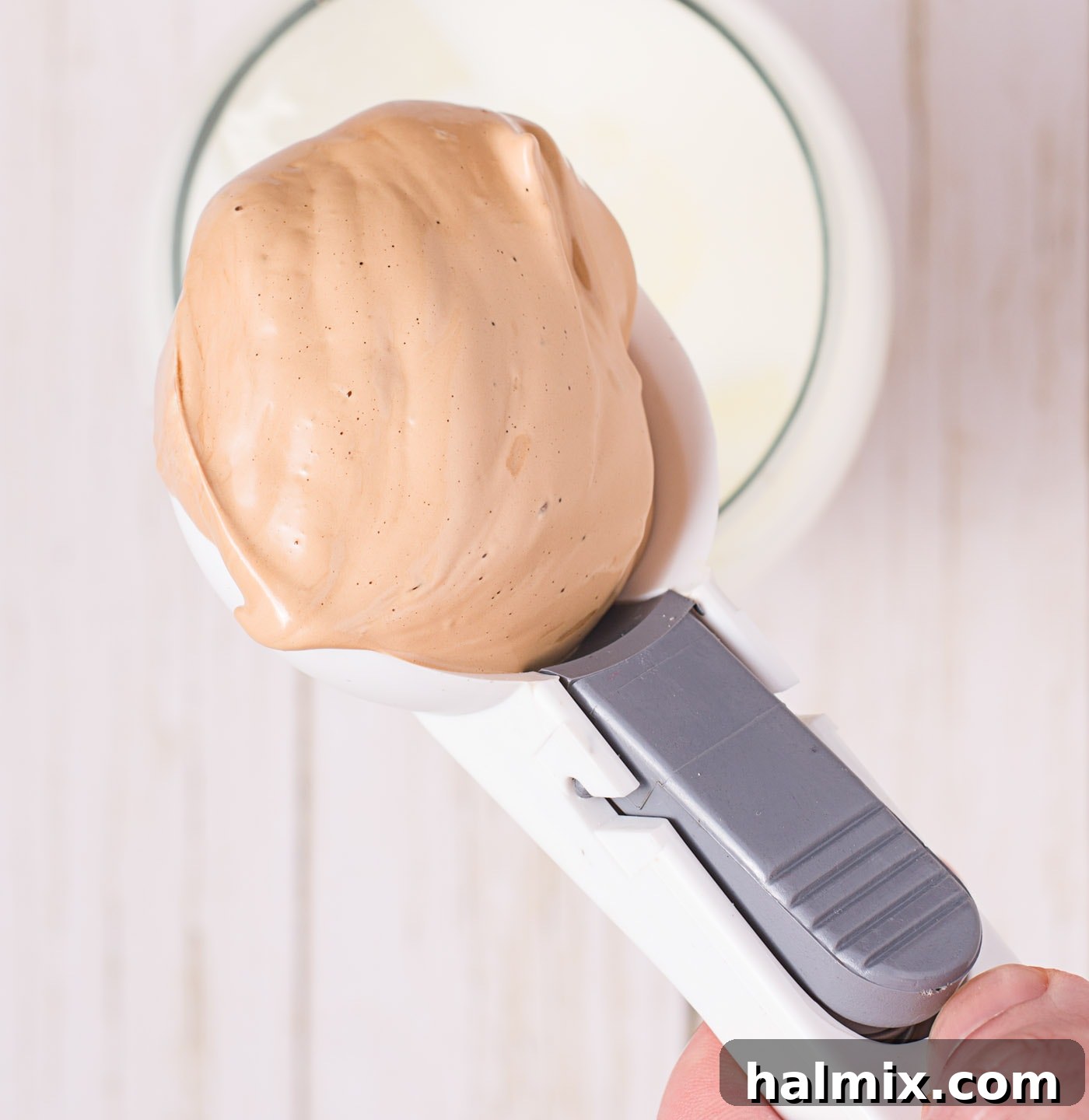 A hand scooping frothy Dalgona coffee cream onto a glass of milk and ice.