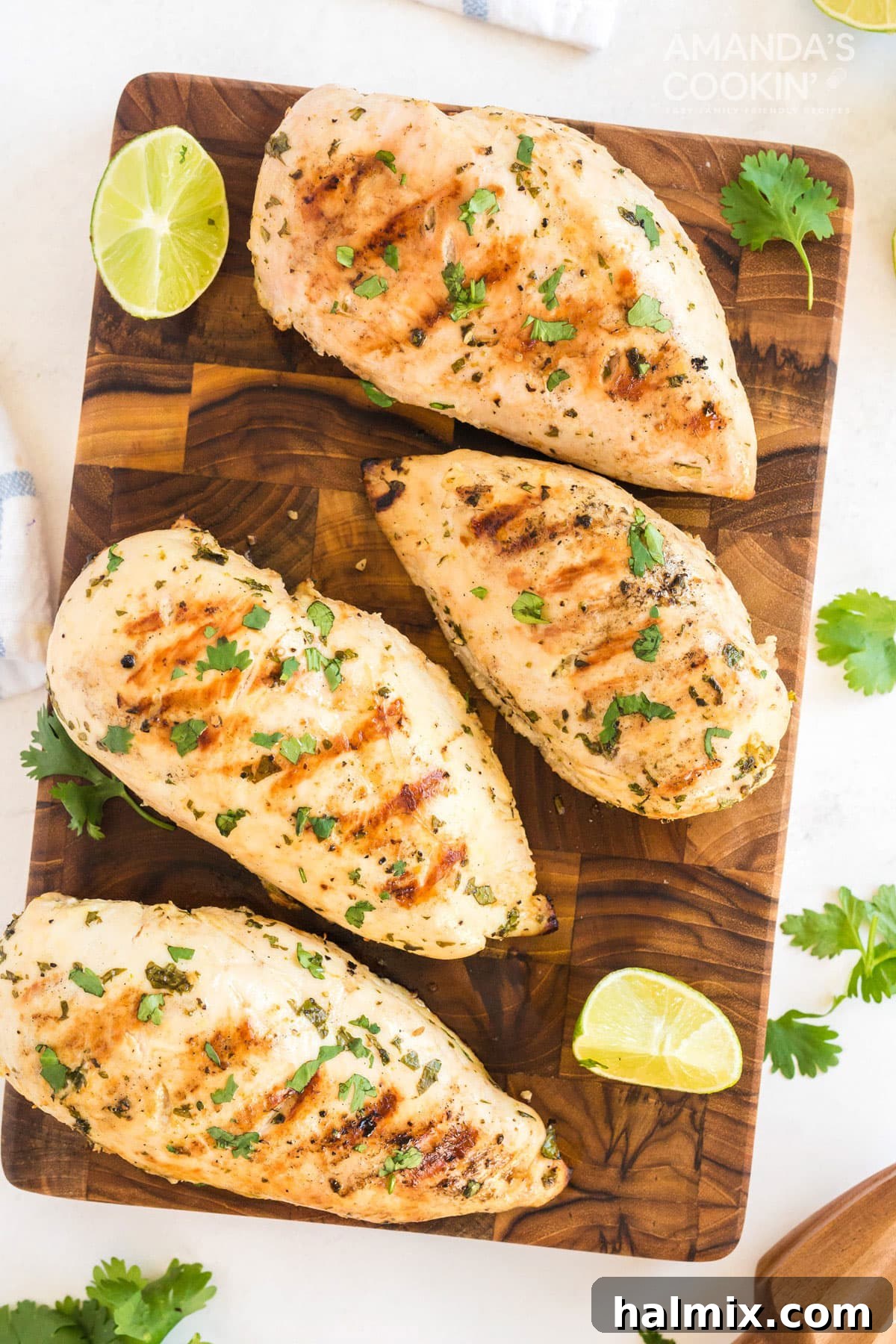 Grilled cilantro lime chicken breasts on a rustic wood cutting board, garnished with fresh cilantro and lime wedges.