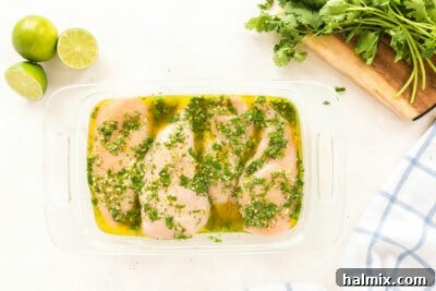 Woman pouring fresh cilantro lime marinade over chicken breasts in a glass dish.