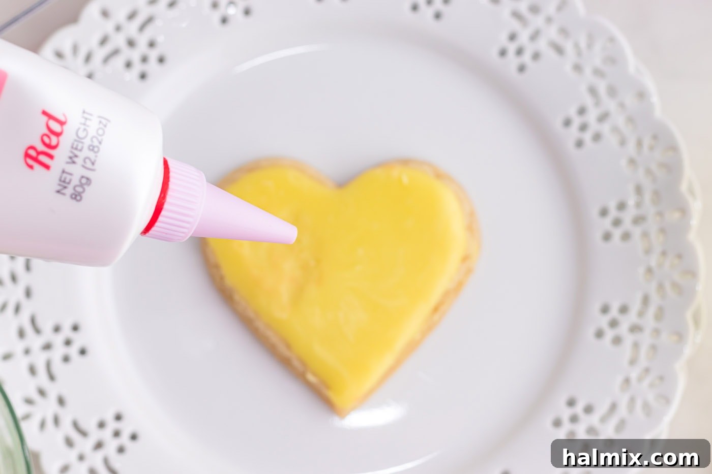 Red gel frosting piping a message onto a pink heart-shaped cookie