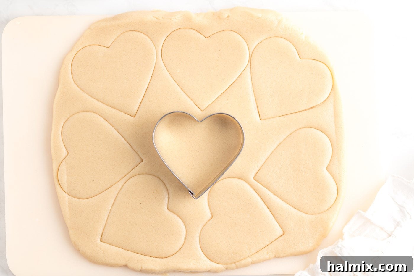 Heart shaped cookie cutter pressing into sugar cookie dough on a floured surface