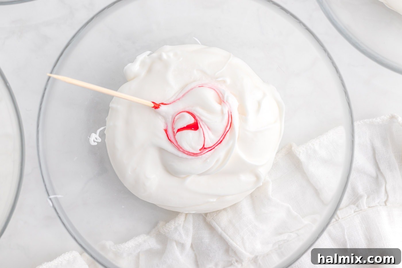 A toothpick mixing red gel food coloring into white frosting in a small bowl