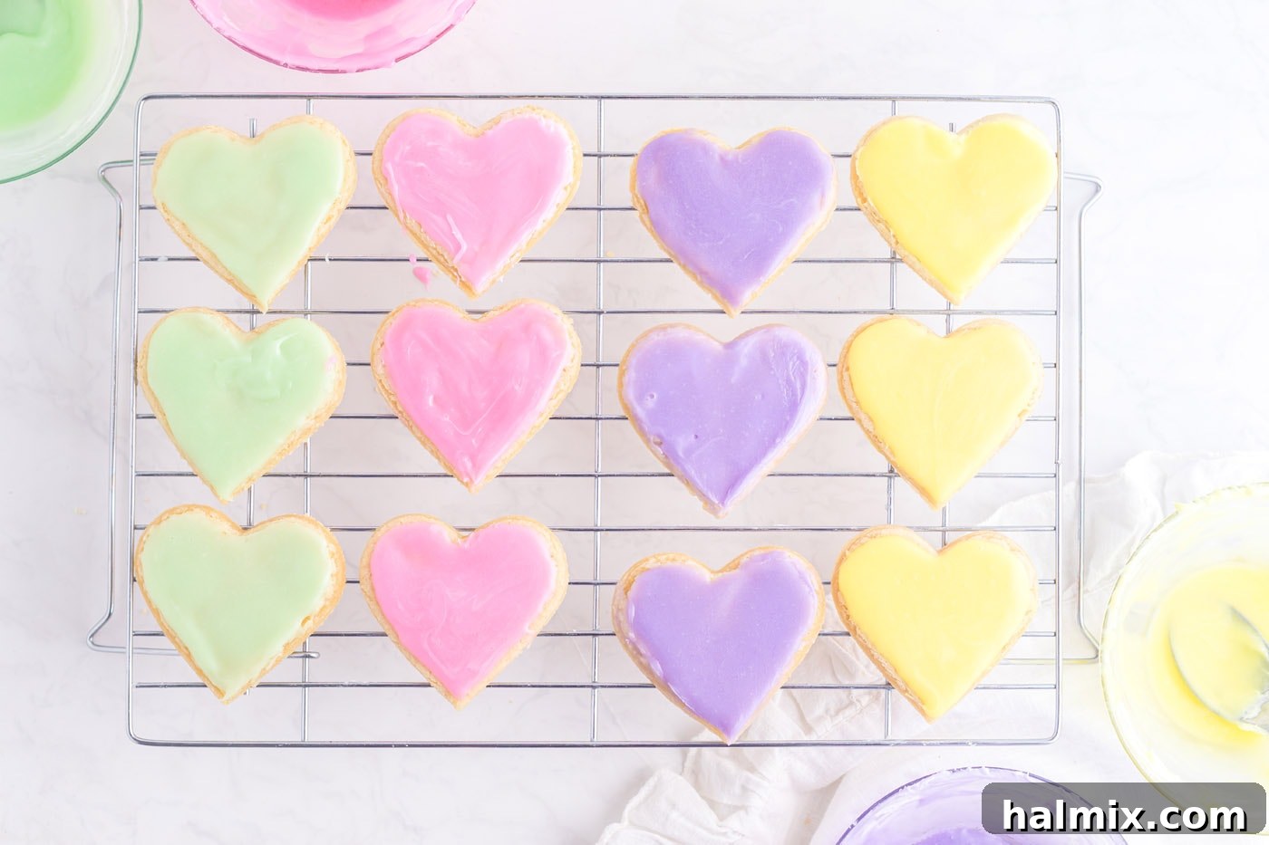 A tray of pastel-colored heart-shaped sugar cookies with a smooth, set frosting base