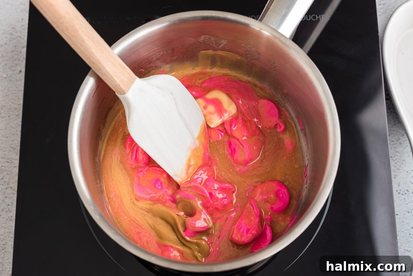 Rubber spatula stirring pink candy melts with peanut butter in a saucepan
