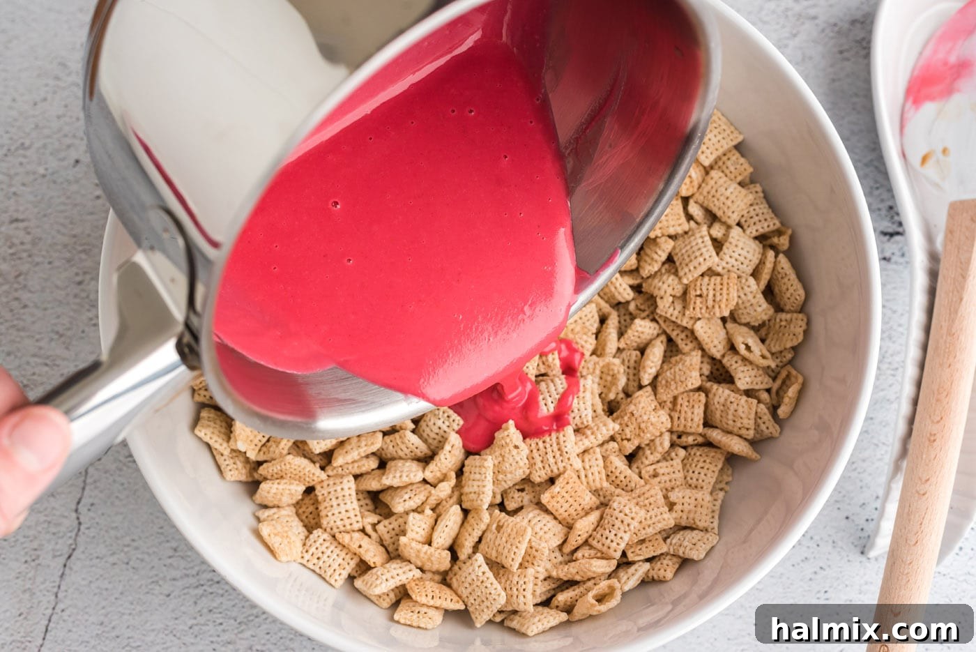 Pouring pink chocolate mixture over Chex cereal in a bowl