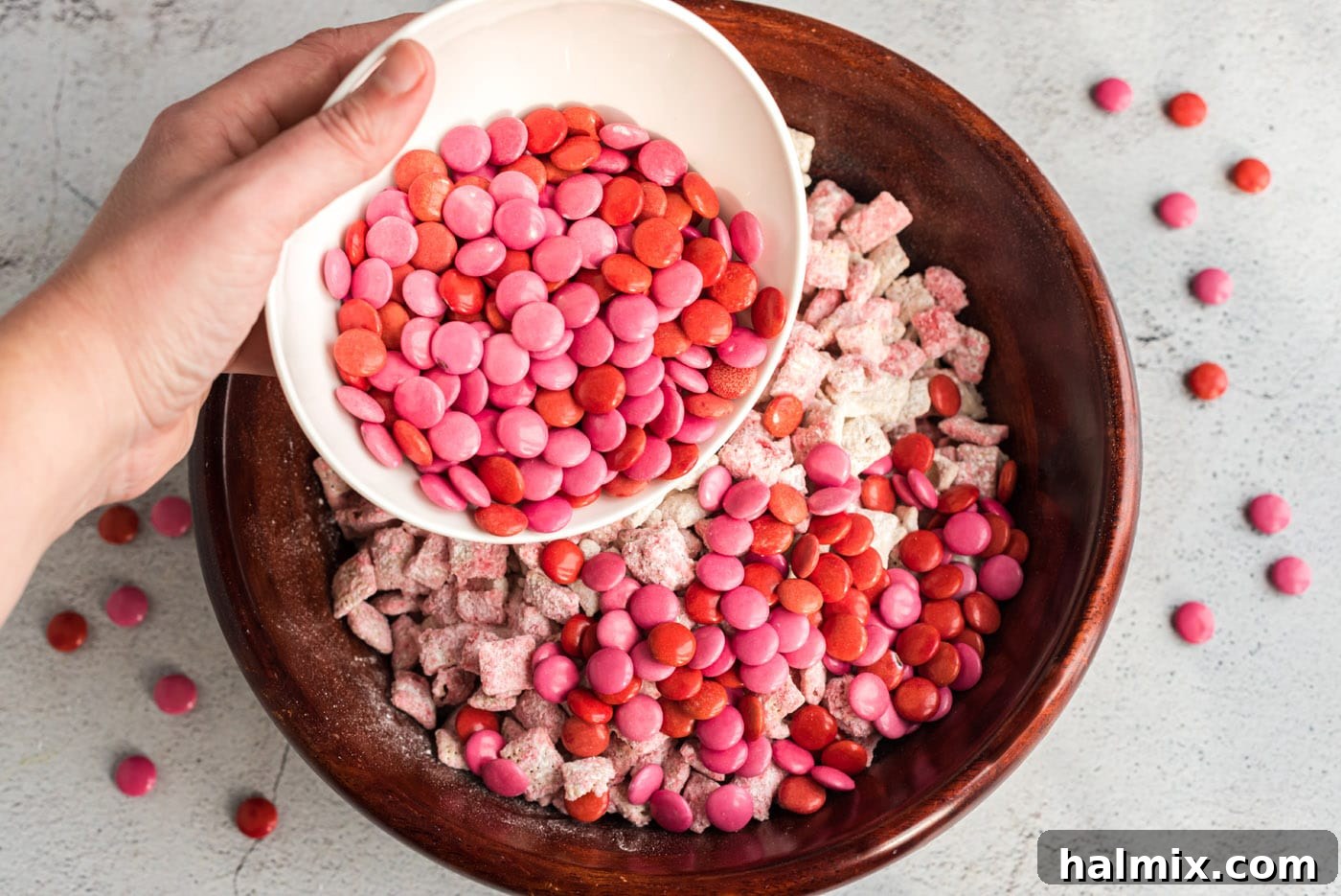 Pouring pink and red M&M's into a bowl of puppy chow