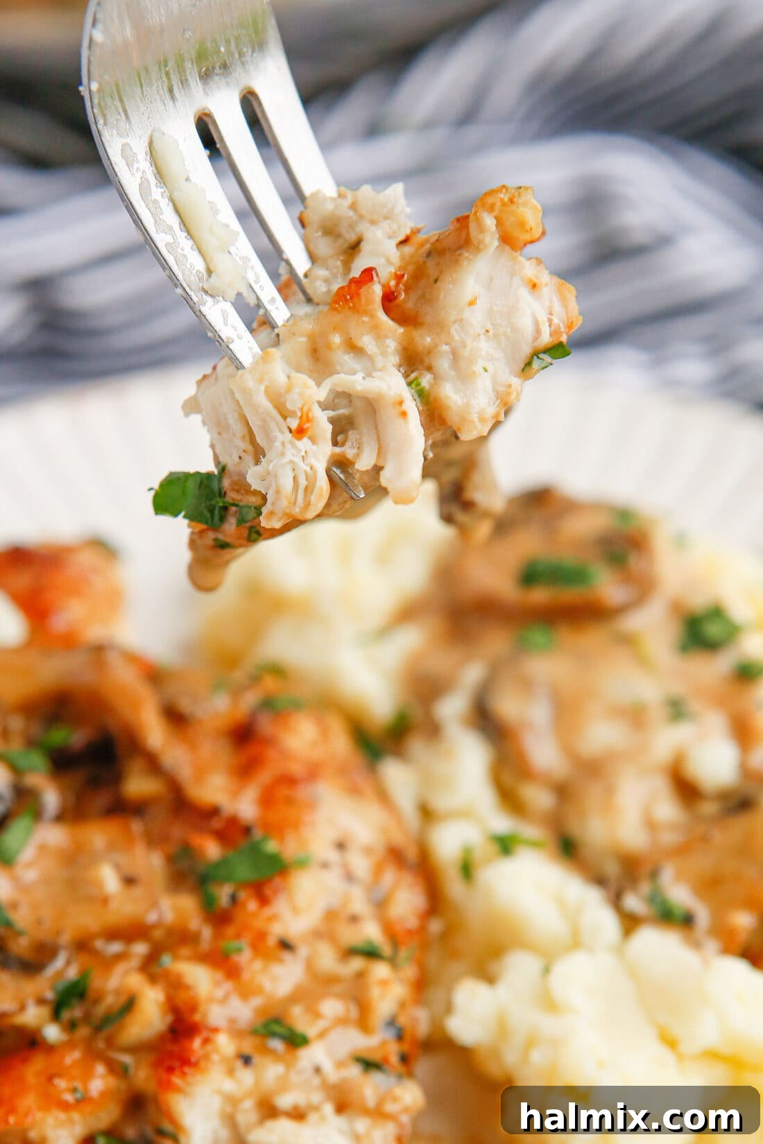 A fork holding a piece of Chicken Marsala with sauce and mushrooms.