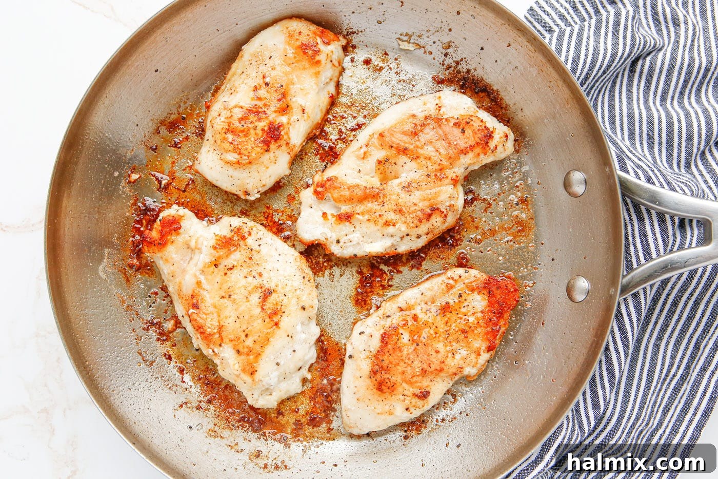 Pan-fried chicken breasts achieving a golden brown color in the skillet.