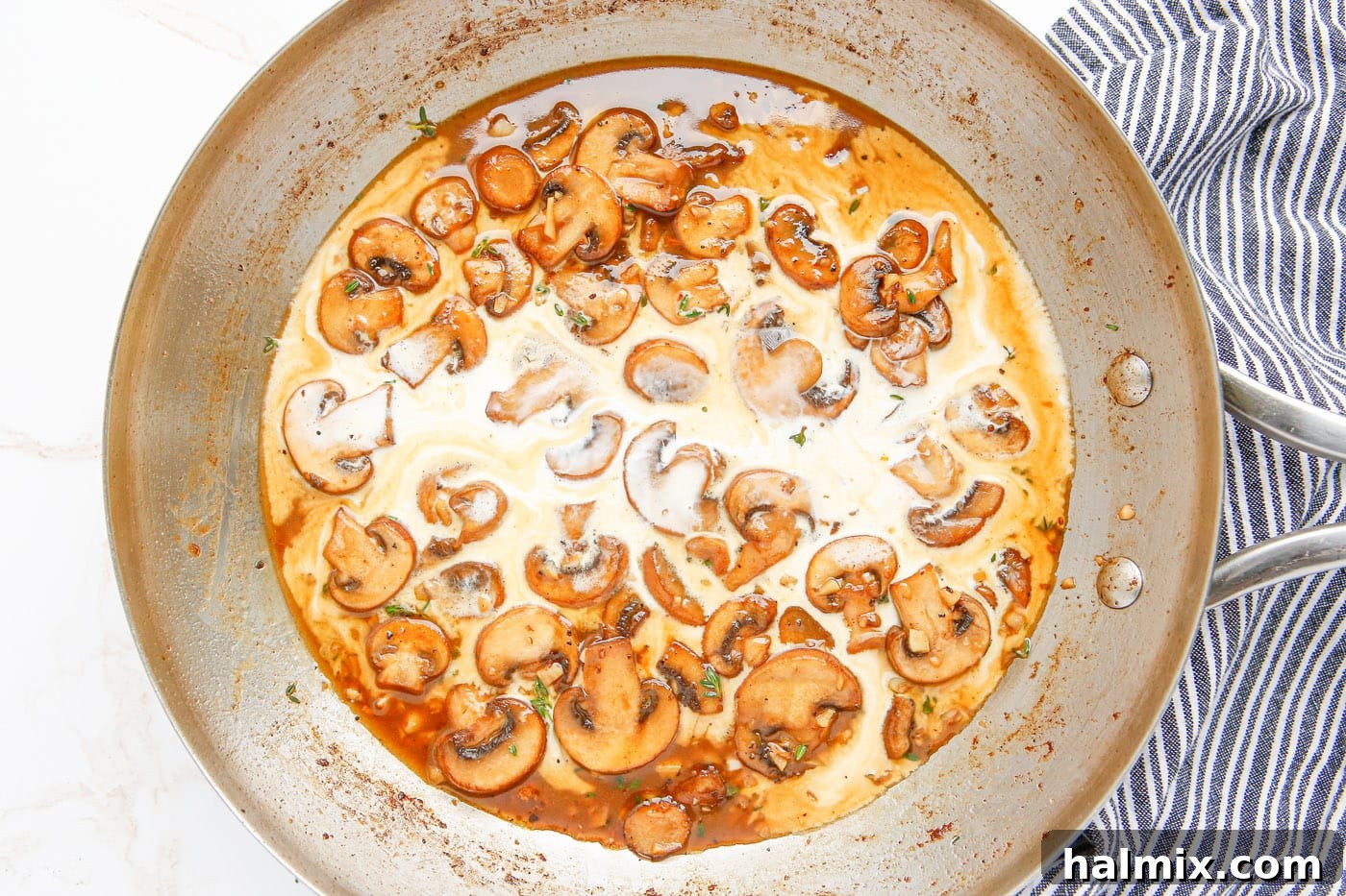 Heavy cream and Marsala wine mixture being added to the sautéed mushrooms in the skillet.