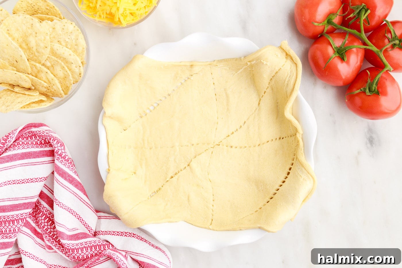 Ultimate Taco Casserole 6 Crescent roll dough being pressed into a 9-inch pie plate to form the crust for the taco pie.