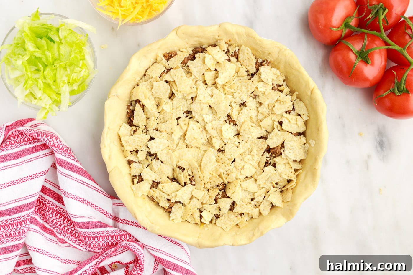 Ultimate Taco Casserole 9 Crushed tortilla chips being layered over the seasoned ground beef in the taco pie.