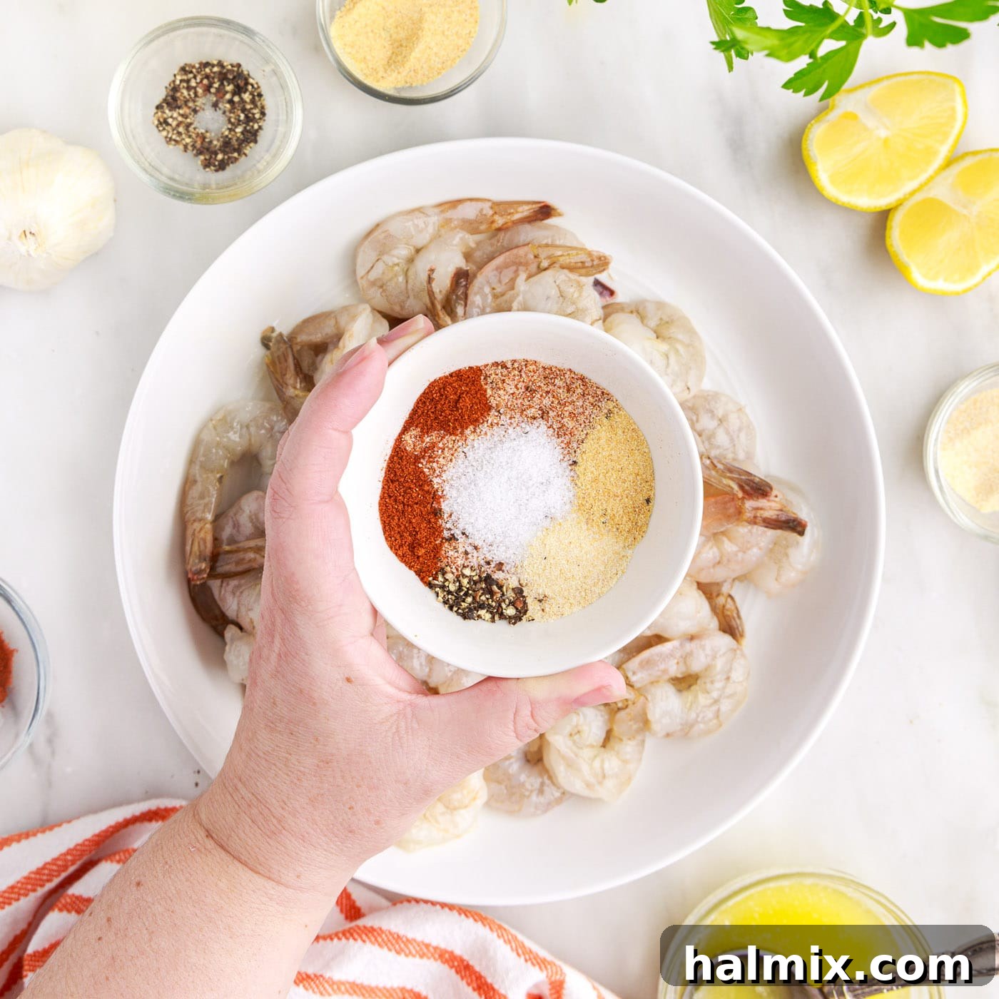 Crispy Air Fryer Shrimp 7 Sprinkling a mixture of spices over butter-coated shrimp in a bowl.