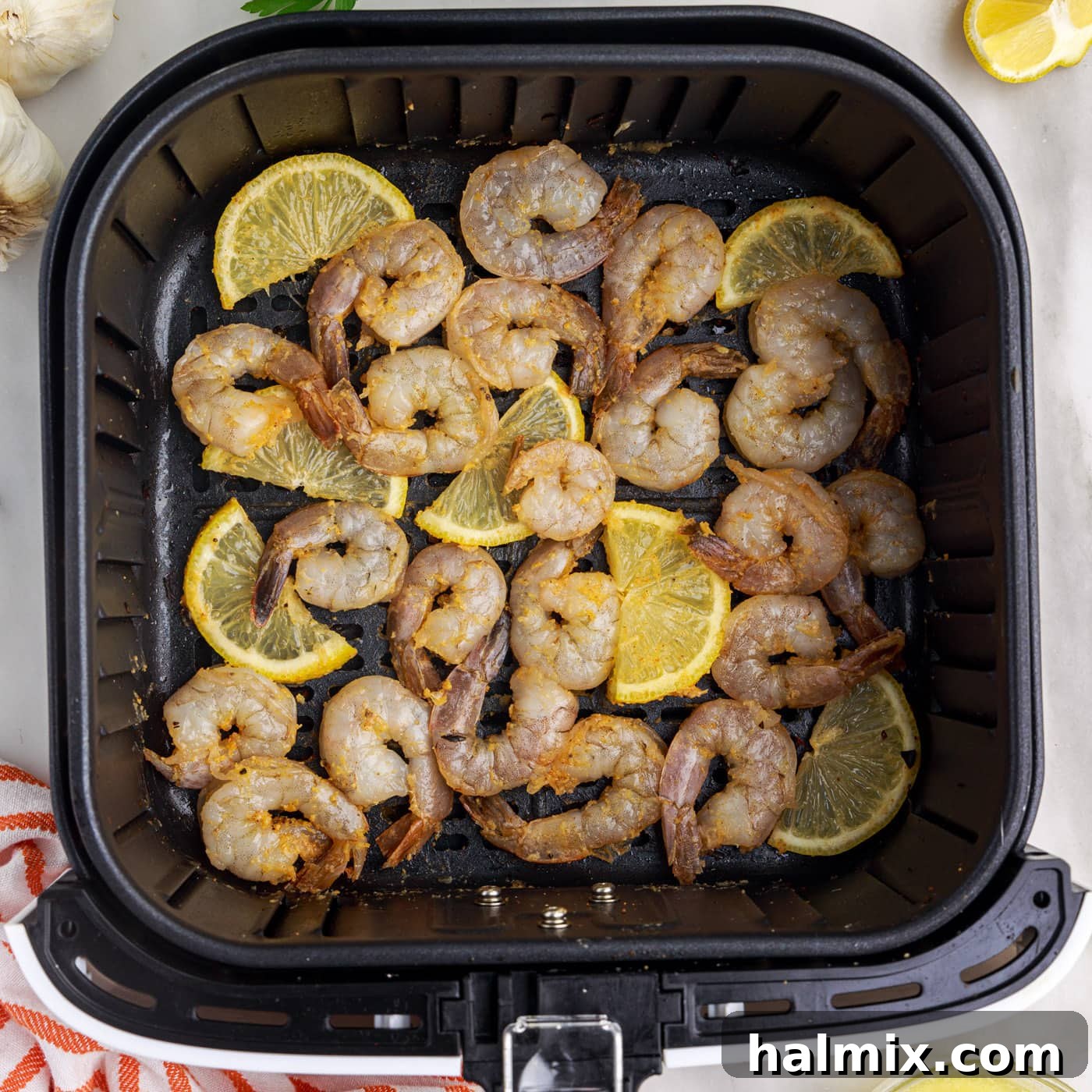 Crispy Air Fryer Shrimp 10 Raw seasoned shrimp and lemon slices arranged in a single layer in an air fryer basket.