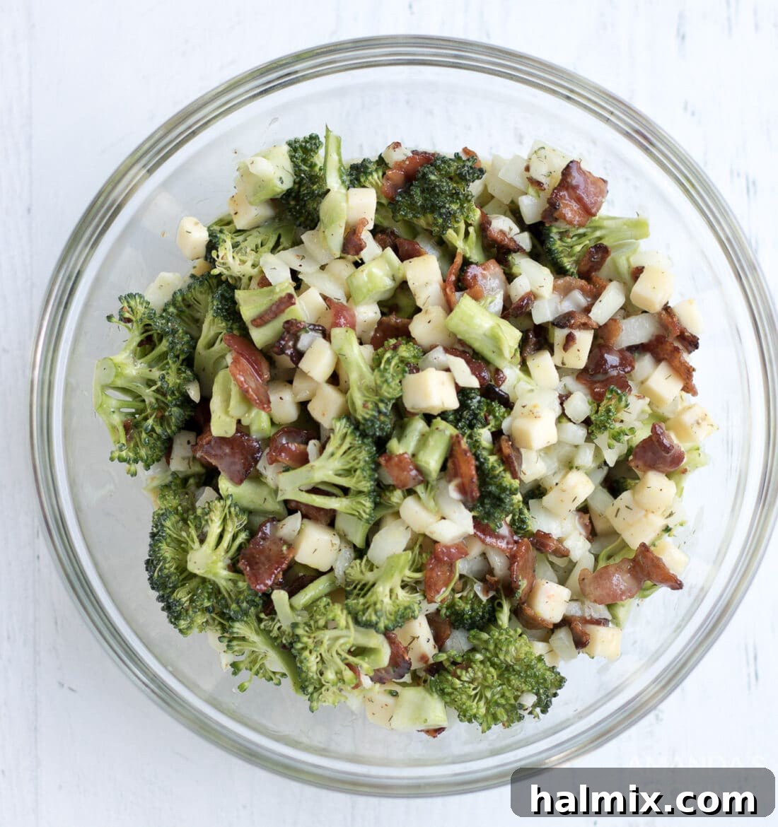 This broccoli salad is a fresh mixture of broccoli, bacon, cheese, and onion. Bring this staple dish to your next potluck or family gathering! A large glass bowl filled with the finished broccoli salad, featuring a rich, creamy texture and colorful ingredients, ready for serving.