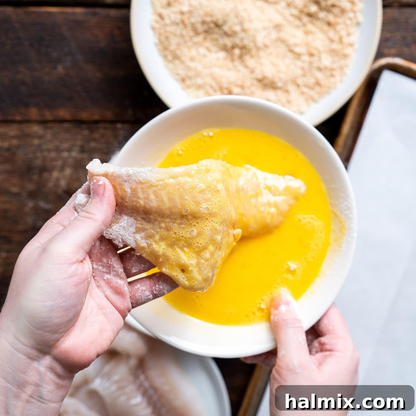 Dipping a cod fillet into the beaten egg wash