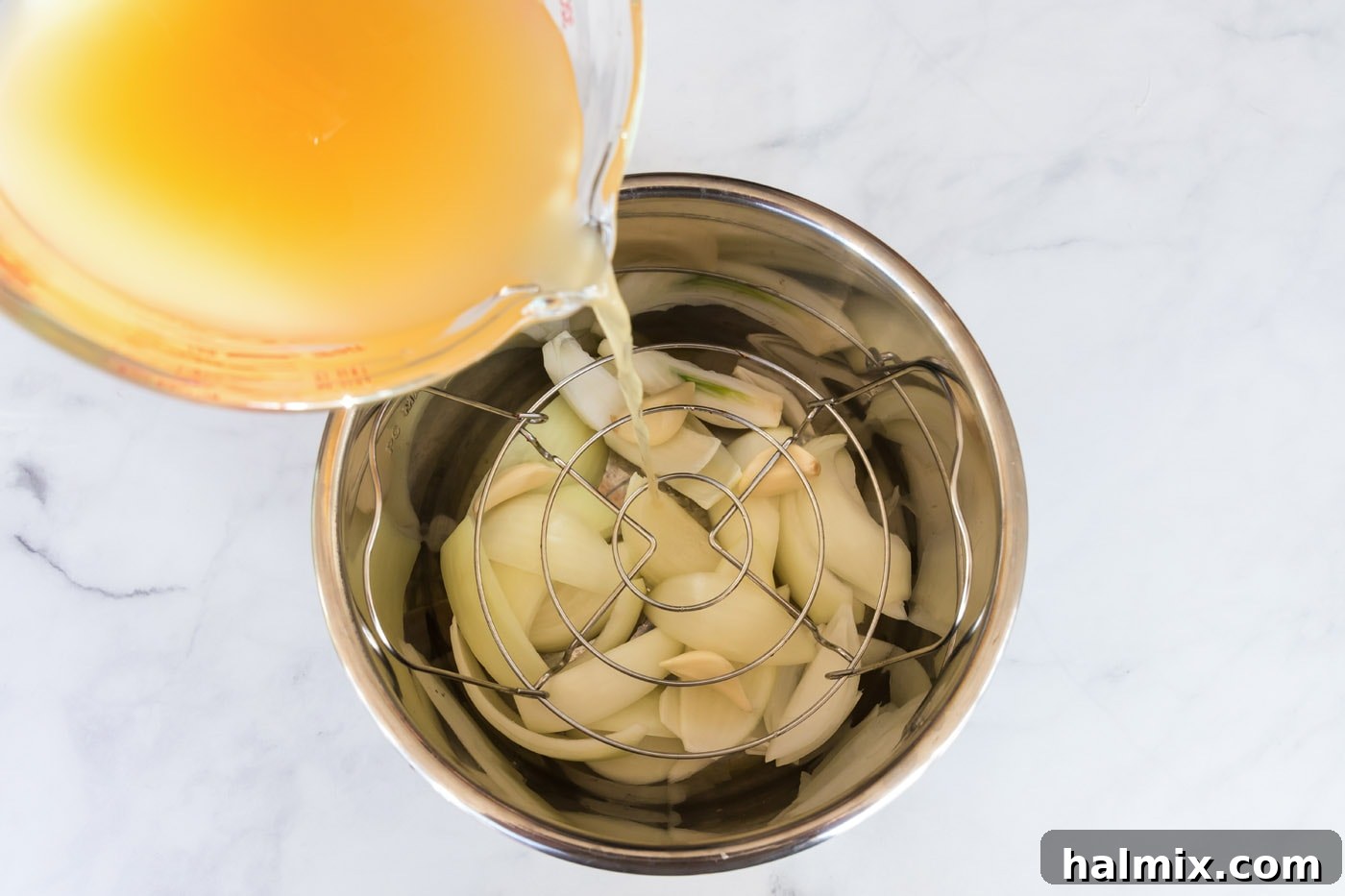 Broth being poured over onion wedges and garlic cloves