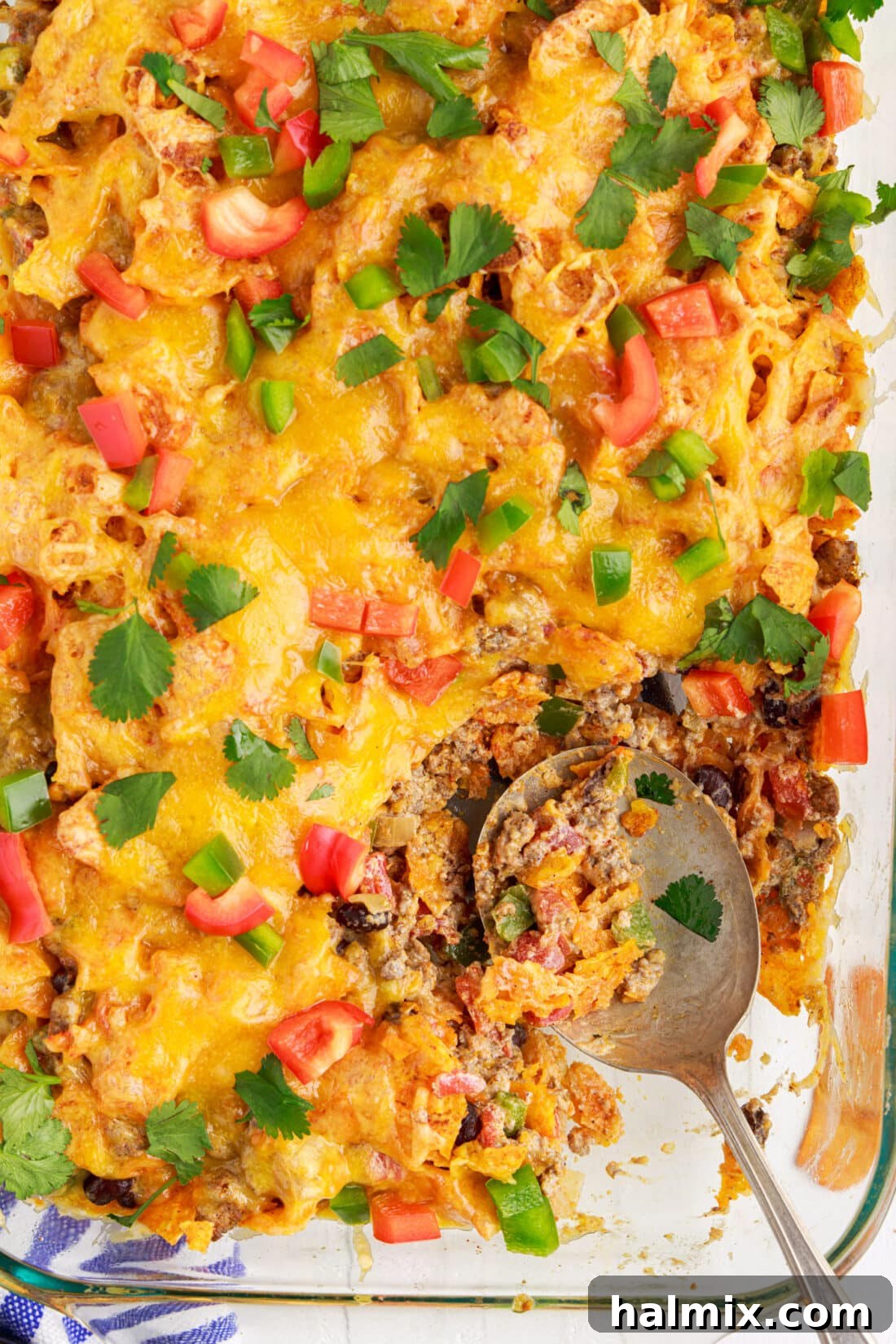 A serving spoon lifting a scoop of cheesy, beefy Dorito Casserole from a baking dish.