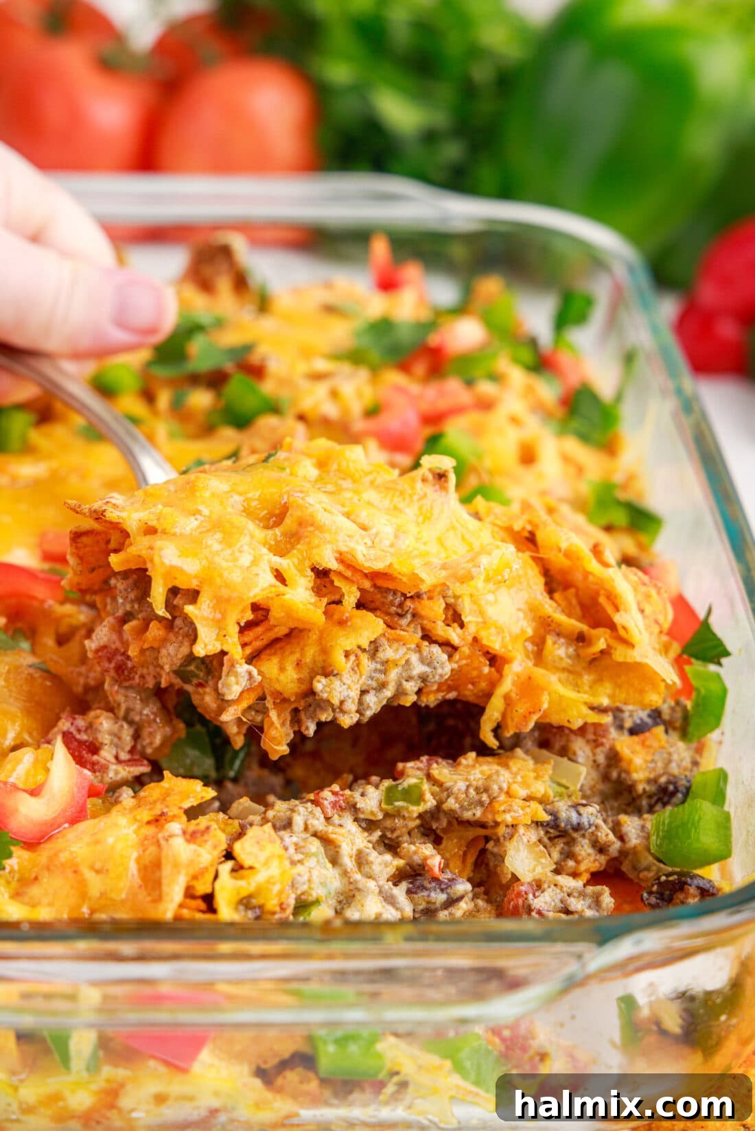 Lifting out a generous serving of cheesy Dorito Casserole with a spoon, showing the layers.