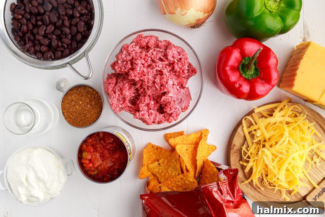 A collection of ingredients laid out for making Dorito Casserole, including chips, ground beef, vegetables, and cheese.