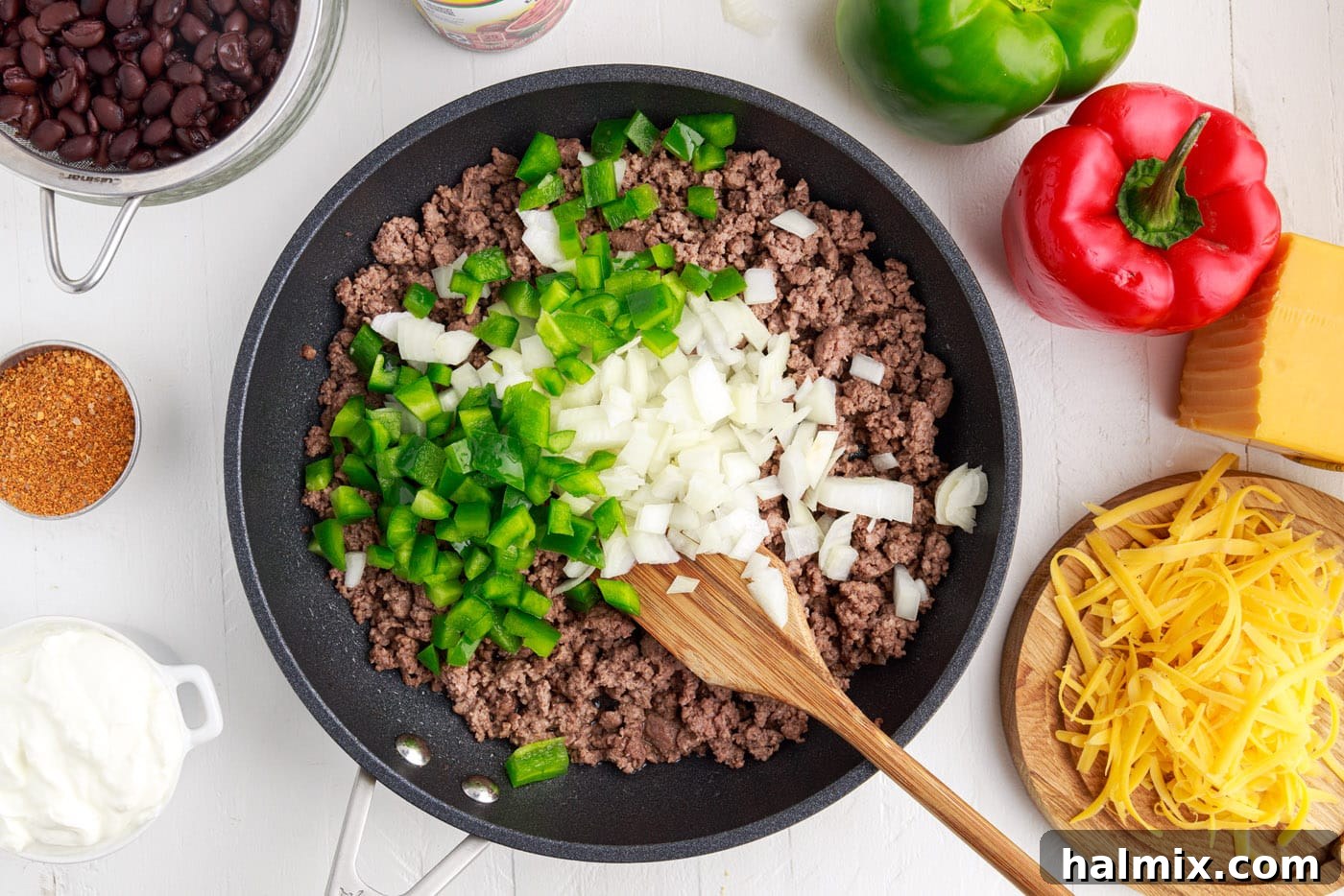 Ground beef with diced onion and bell pepper cooking in a large skillet.