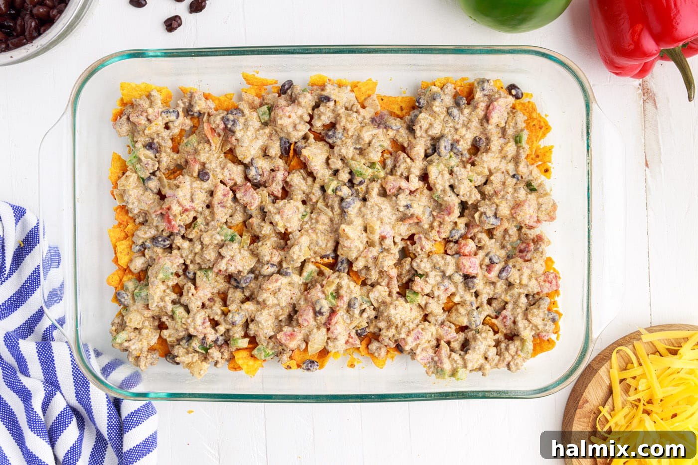 Half of the ground beef mixture spread over crushed Doritos in a casserole dish.