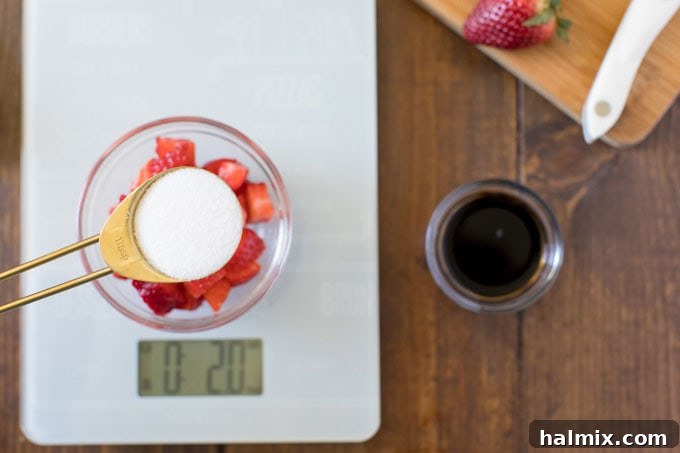 measuring spoon with sugar hovering over bowl of strawberries on a kitchen scale