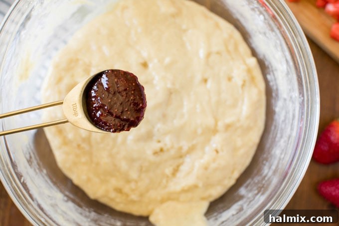 spoon of homemade strawberry jam hovering over bowl of muffin batter