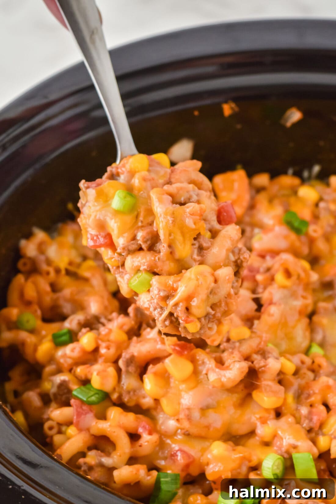 Close-up of a spoon scooping a portion of Crockpot Ground Beef Casserole, highlighting the melted cheese and pasta.